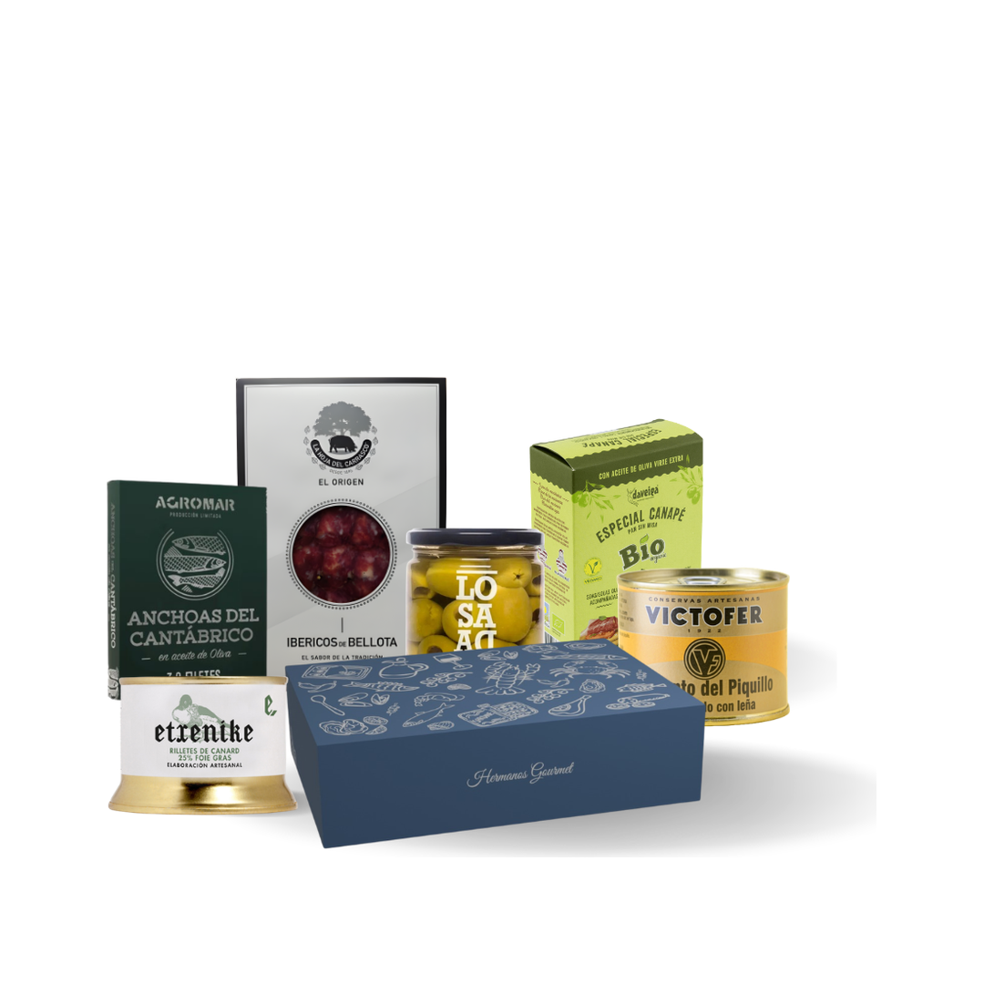 Contenido de la caja regalo de aperitivo: anchoas del Cantábrico, salchichón ibérico, rillettes de pato, pimientos del piquillo, tostas para canapés y aceitunas Manzanilla junto a la caja azul oscuro de Hermanos Gourmet