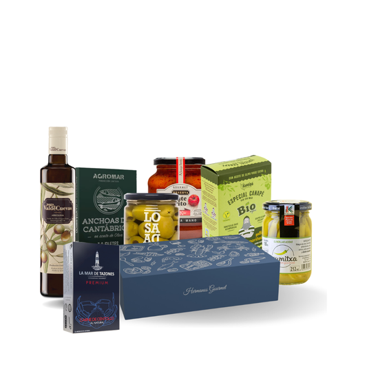 Premium gift box contents: spider crab, Cantabrian anchovies, Arbequina olive oil, piparras, fried tomato sauce, canapé toasts and Manzanilla olives beside the dark blue Hermanos Gourmet gift box