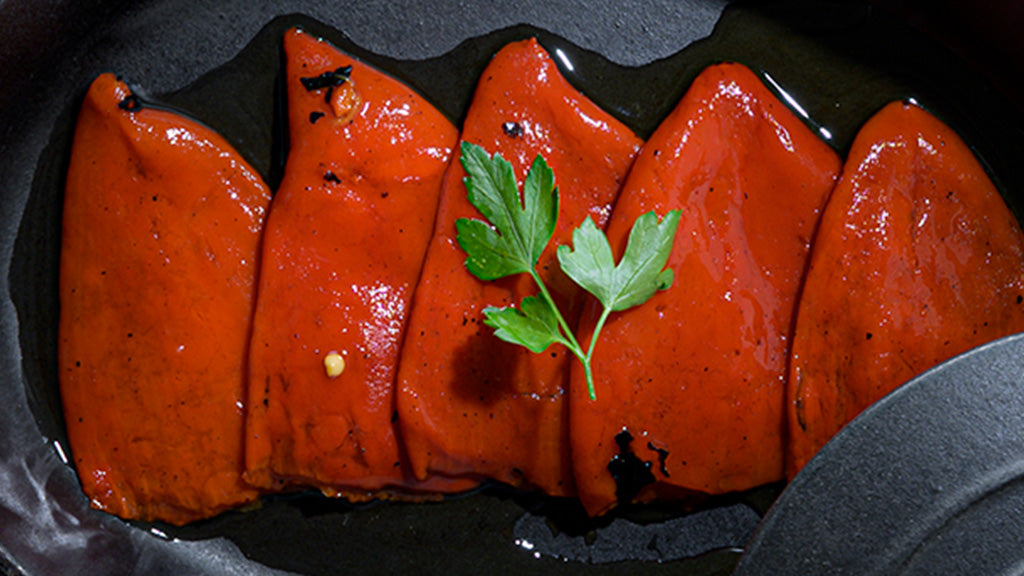 Roasted piquillo pepper fillets served on a dark plate in their own oil, with flat-leaf parsley